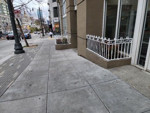 A sidewalk in front of a building with a white railing.