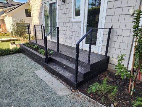 A black deck with stairs and a black railing in front of a white house.
