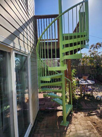 A green spiral staircase is attached to the side of a house.