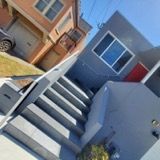 A house with stairs leading up to it and a car parked in front of it.