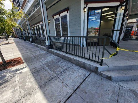 A sidewalk in front of a building with a metal railing.