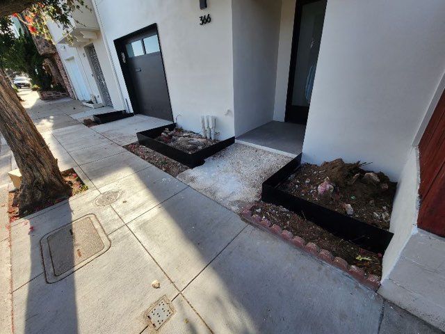 A white house with a black garage door is sitting on a sidewalk next to a tree.