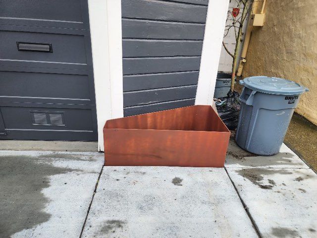 A brown box sits on a sidewalk next to a blue trash can
