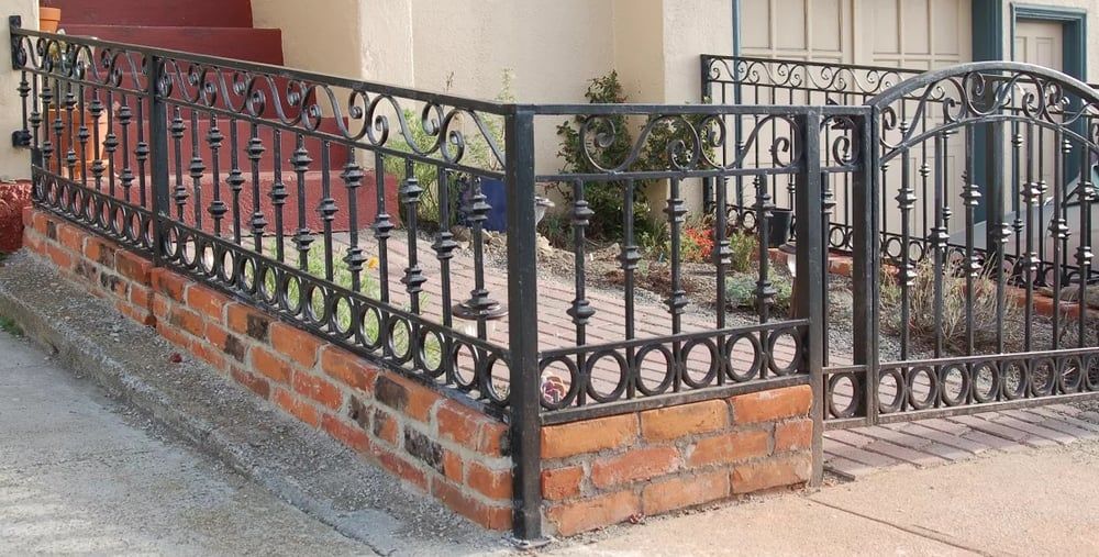 A wrought iron fence is surrounding a brick wall