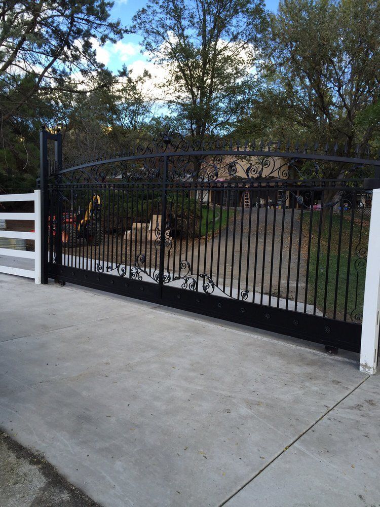 A black sliding gate with a white fence in front of a house.