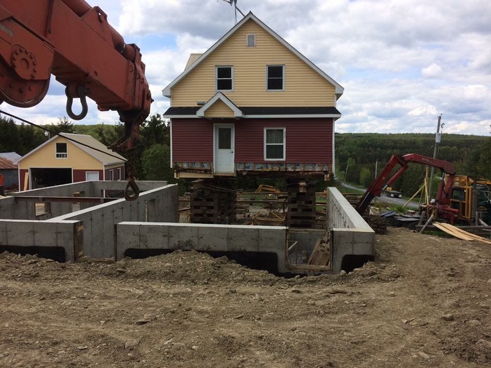 La maison a été soulevée du sol par une grue et s'apprête à être installée sur de nouvelles fondations en béton.