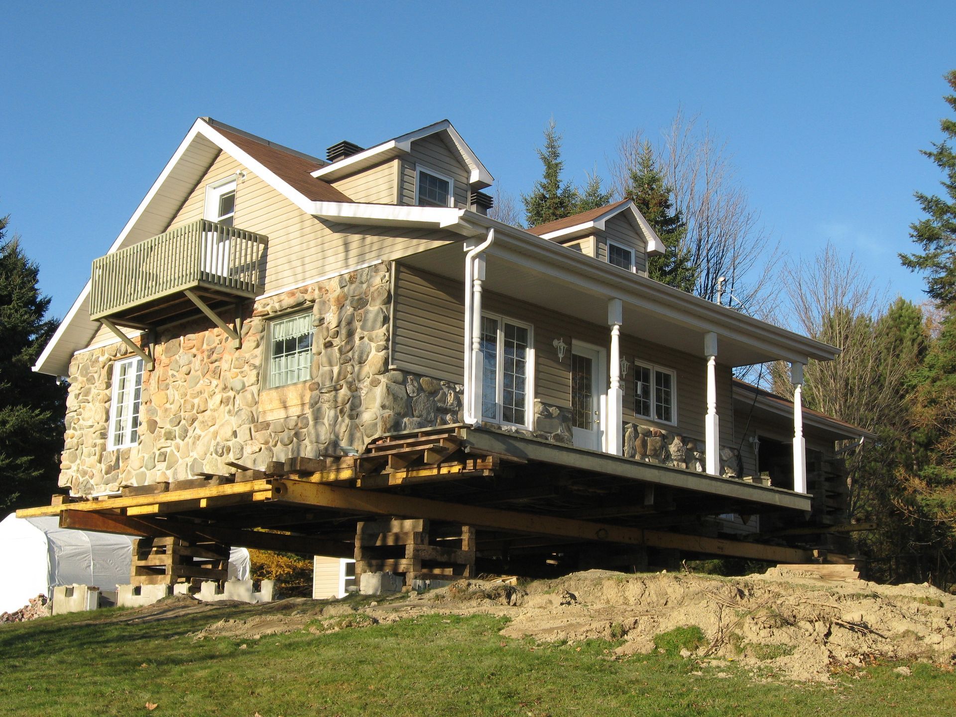 Maison surélevée sur poutres en bois, probablement pour des travaux de fondation, située dans une cour.