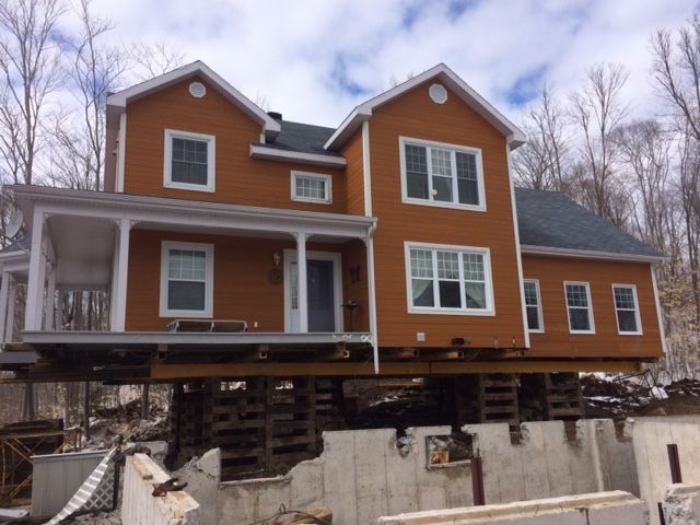 Maison surélevée sur pilotis en bois, extérieur brun, boiseries blanches, porte bleue, ciel couvert.