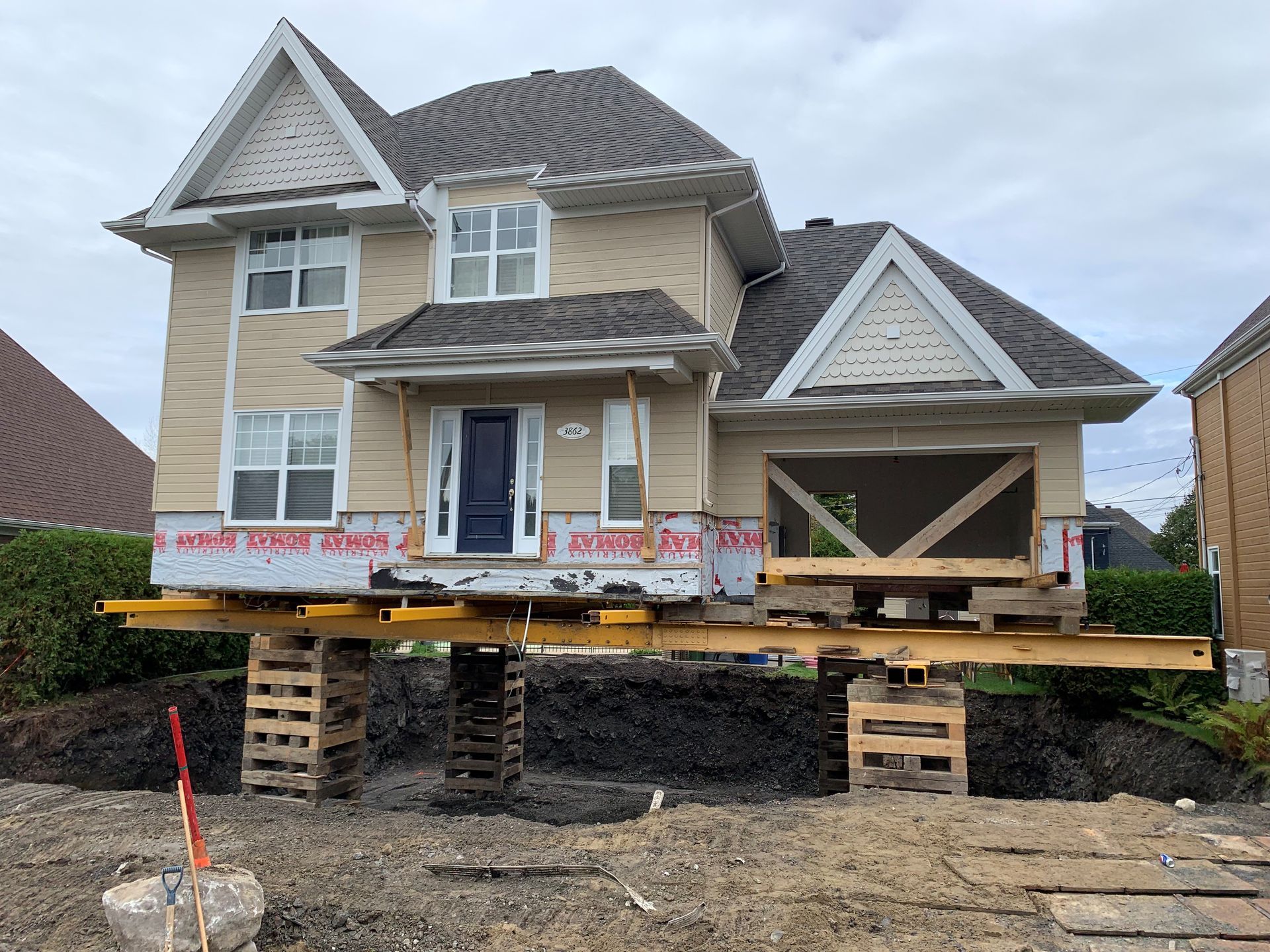 Maison surélevée sur pilotis en bois, en construction, avec un bardage beige et un toit gris.