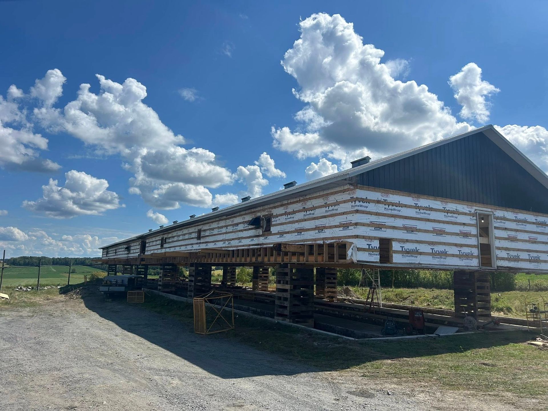 Grange sur des supports temporaires, ciel bleu, nuages et champs en arrière-plan.