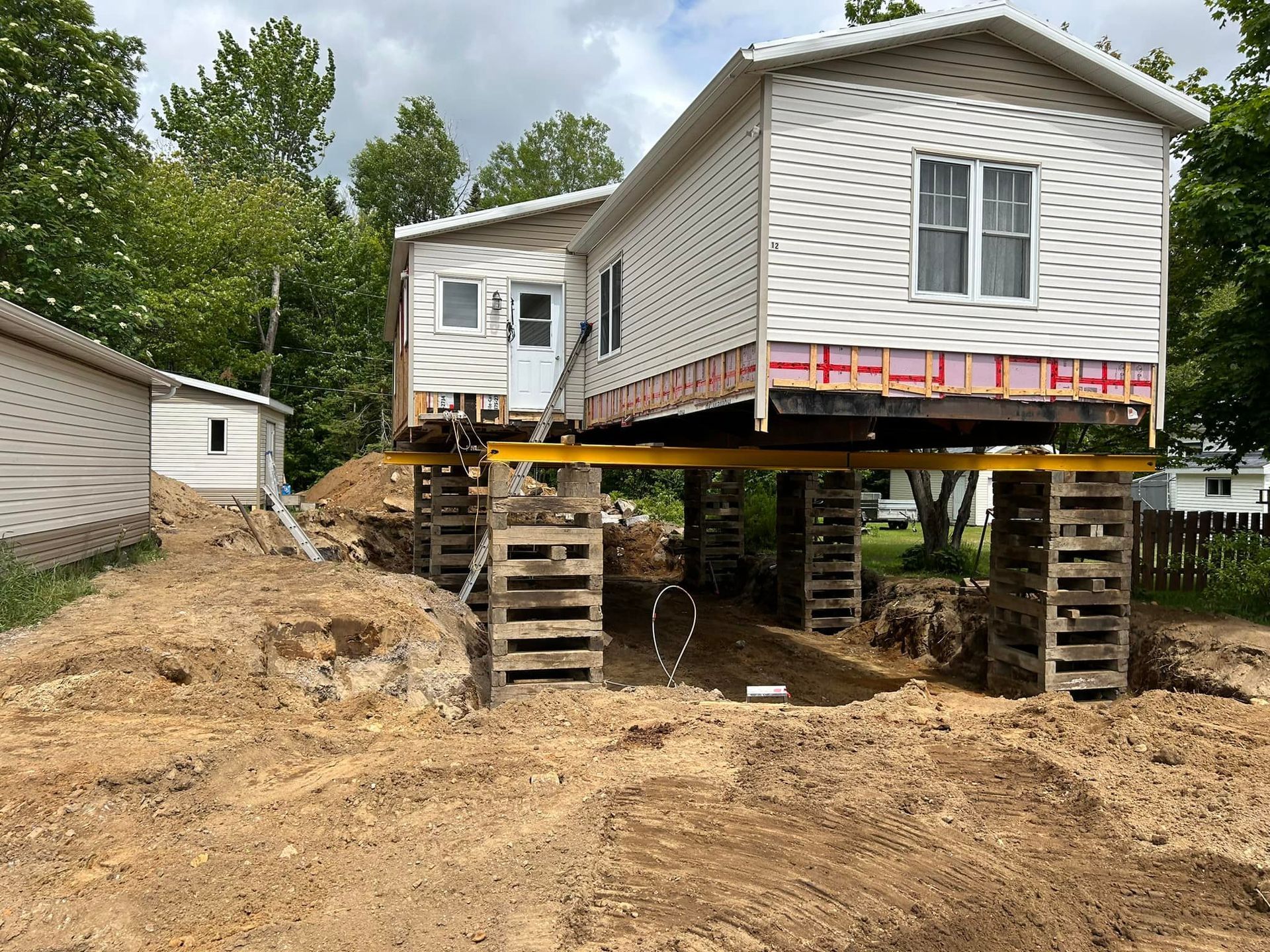 Maison surélevée sur des supports en bois. Chantier avec fondations apparentes.