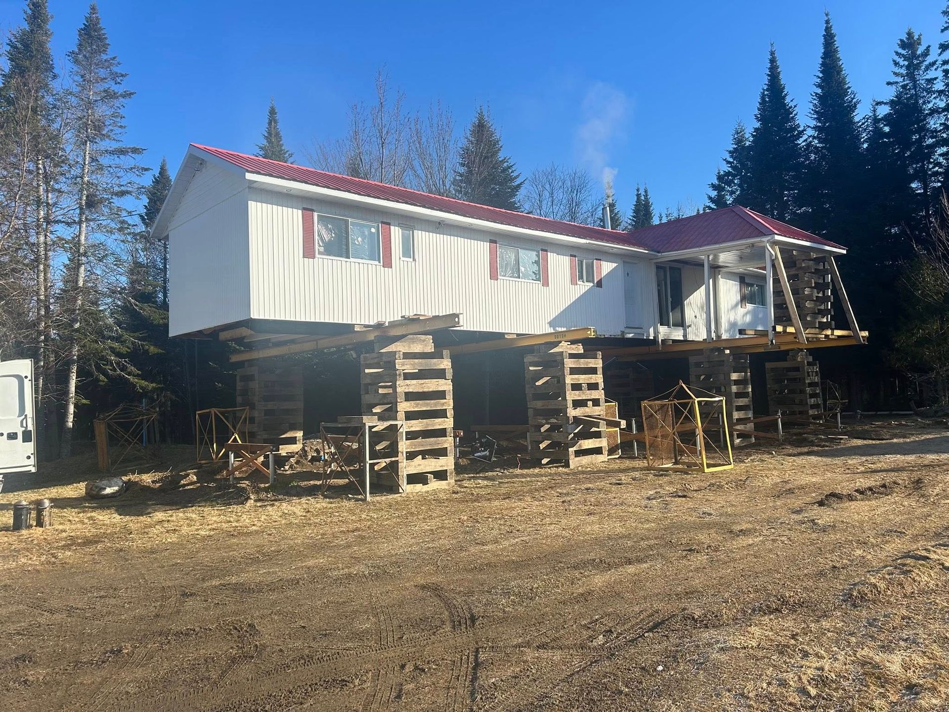Maison blanche sur pilotis, toit et volets rouges. À l'extérieur, arbres en arrière-plan, journée ensoleillée.