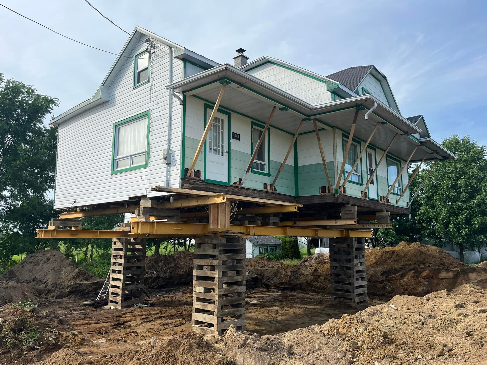 Maison surélevée sur des supports en bois pendant les travaux de fondation sur un terrain en terre.