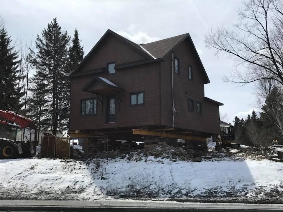 Maison brune surélevée sur des supports en bois, neige au sol.