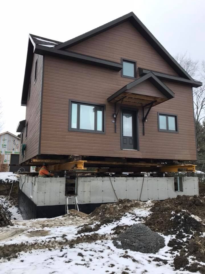 Une maison surélevée sur des vérins au-dessus de nouvelles fondations en béton ; de la neige au sol.