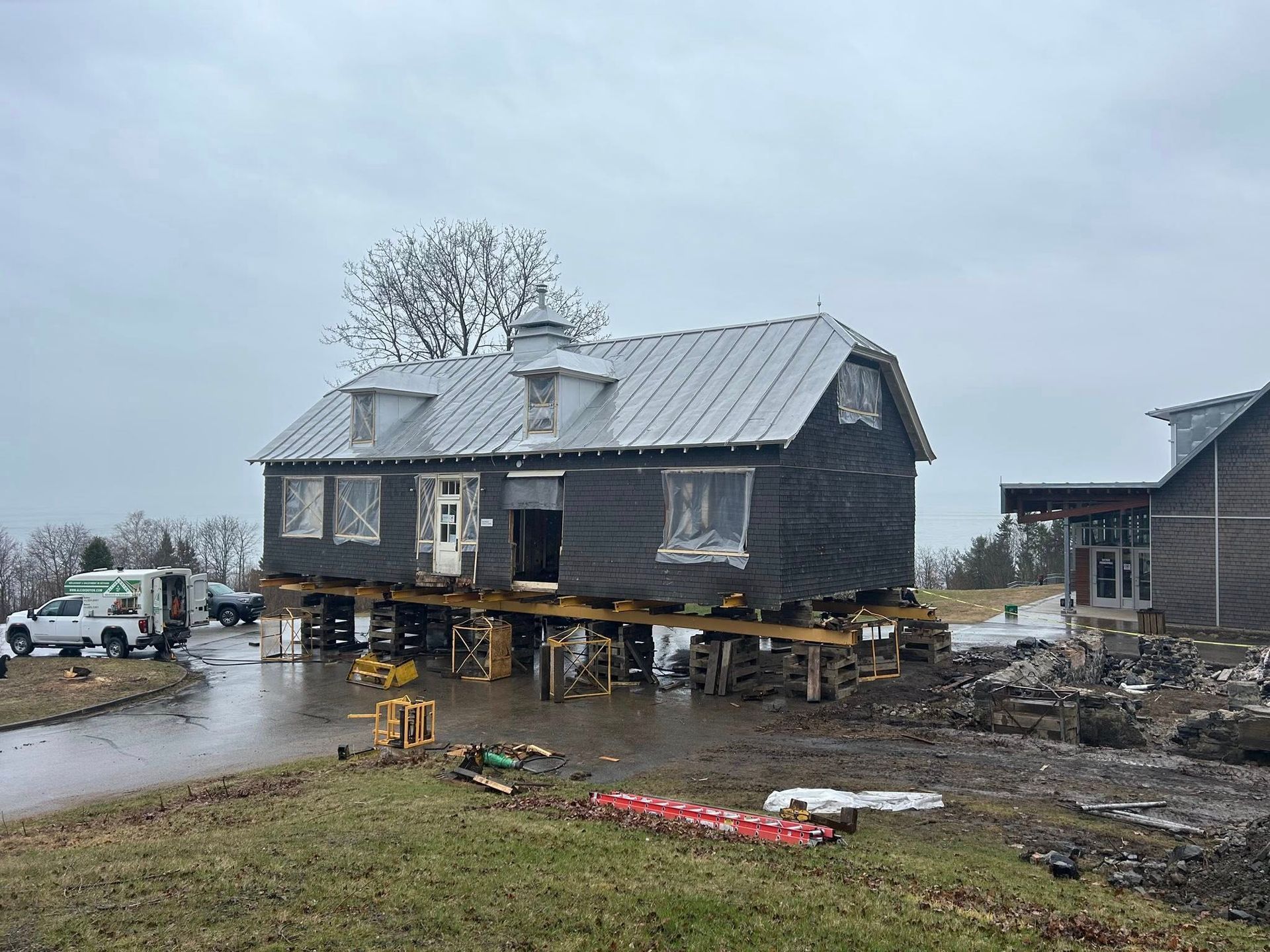 Bâtiment noir sur pilotis en bois ; chantier, journée nuageuse.