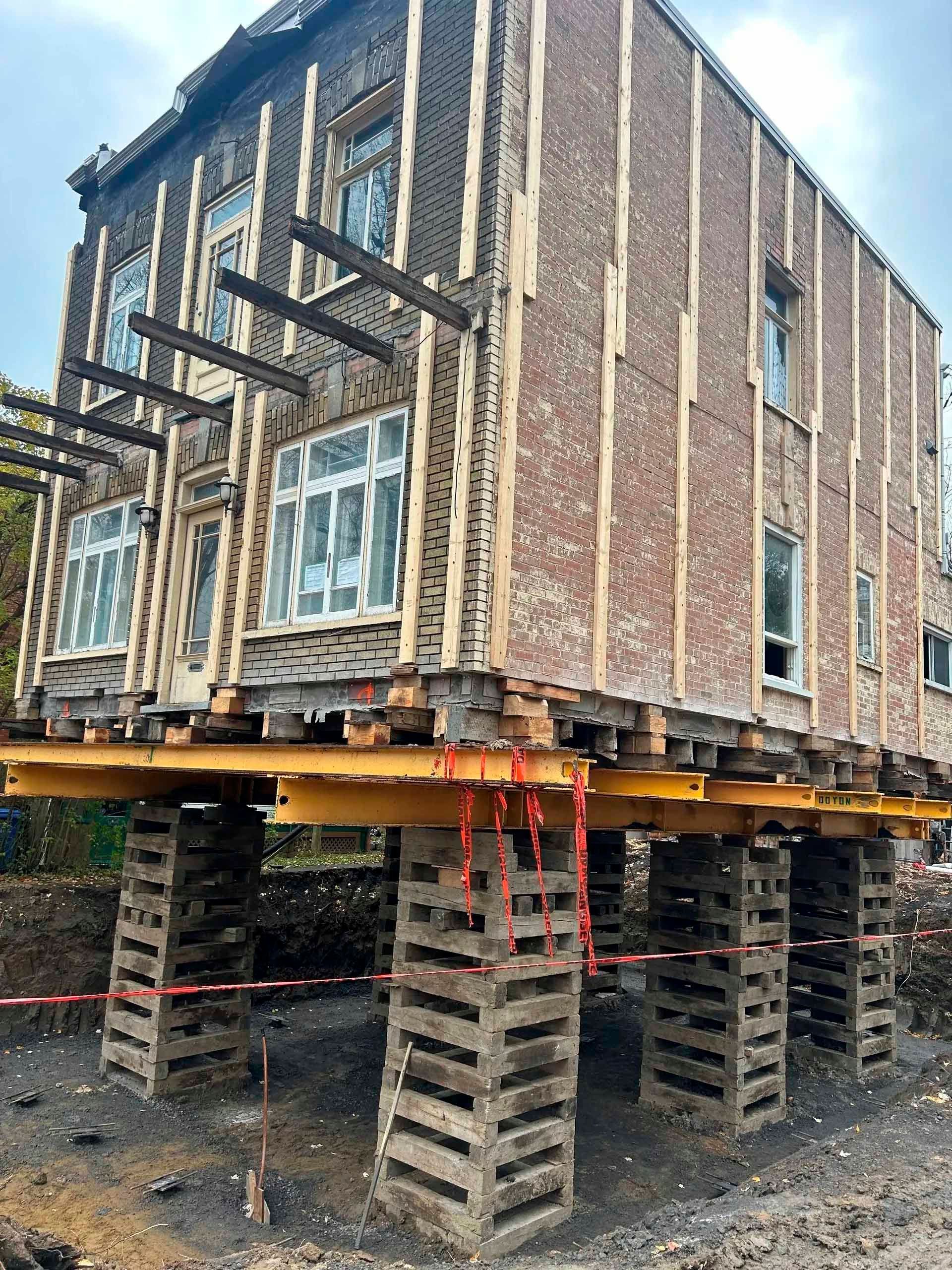 Bâtiment surélevé sur des supports en béton pour un déplacement ou des travaux de fondation.