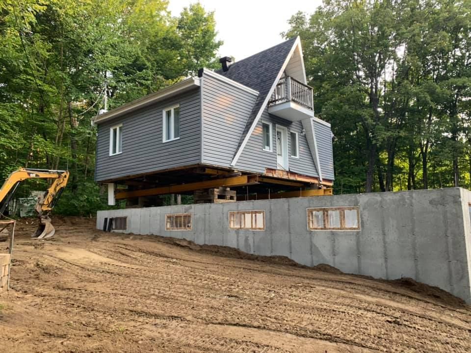 Maison surélevée sur pilotis au-dessus de fondations en béton neuves. Chantier avec pelleteuse.
