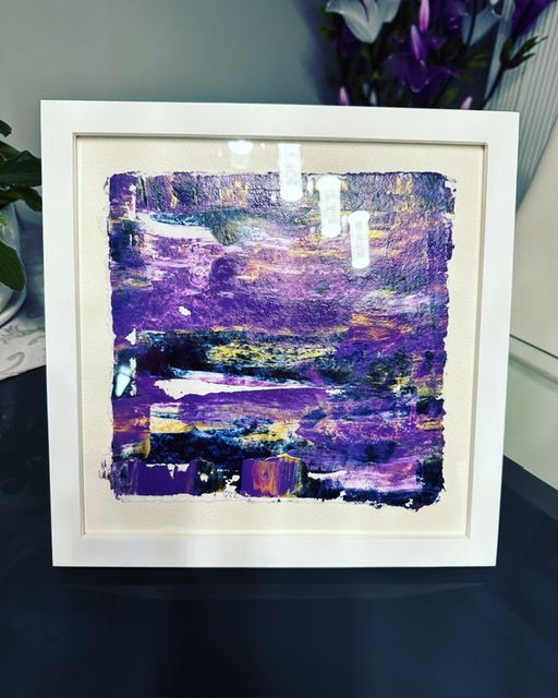 A purple painting in a white frame on a table