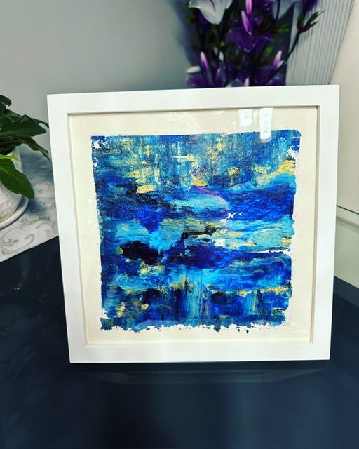 A blue and yellow painting in a white frame on a table