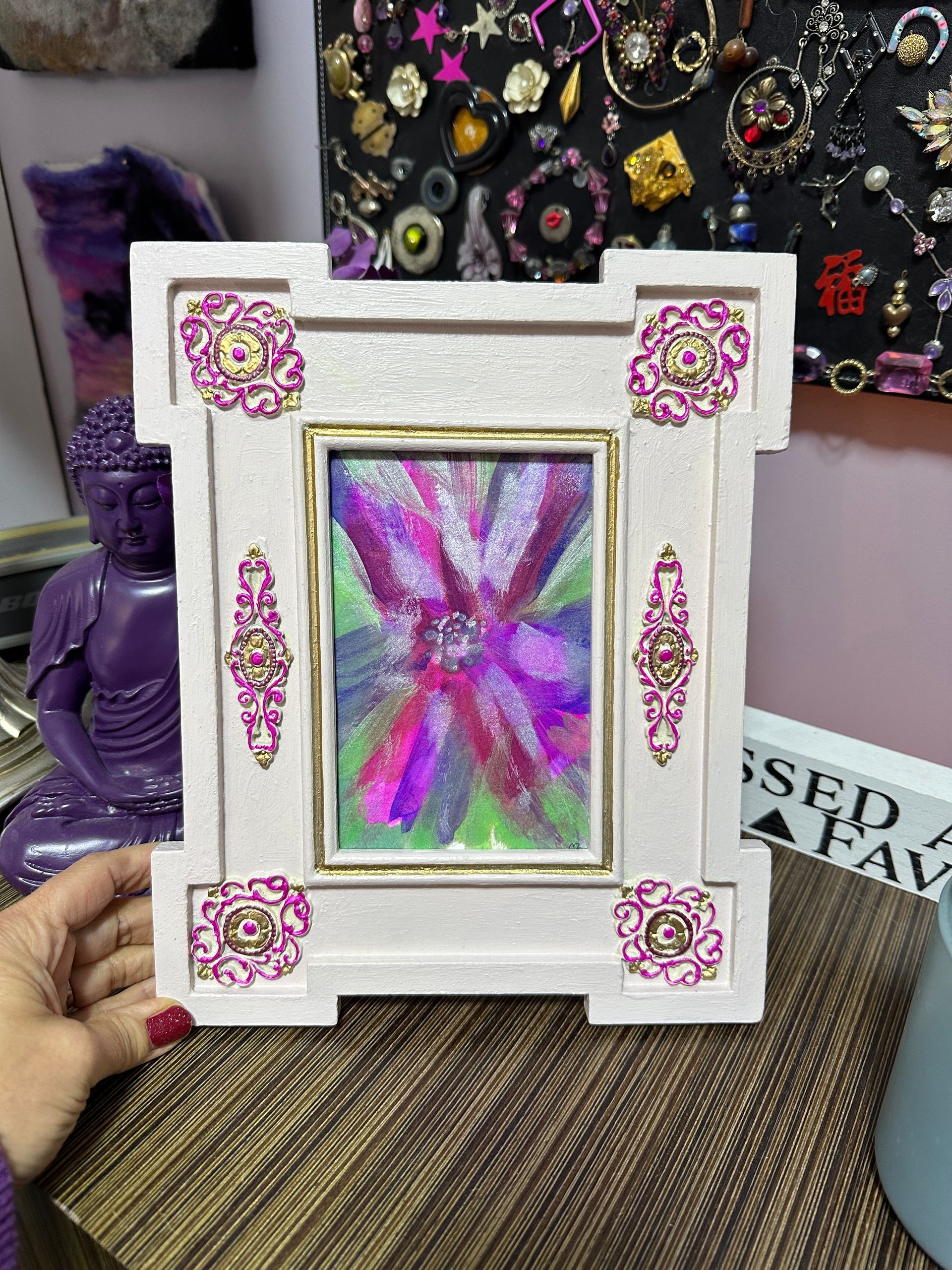 A person is holding a picture frame with a painting of a flower on it.