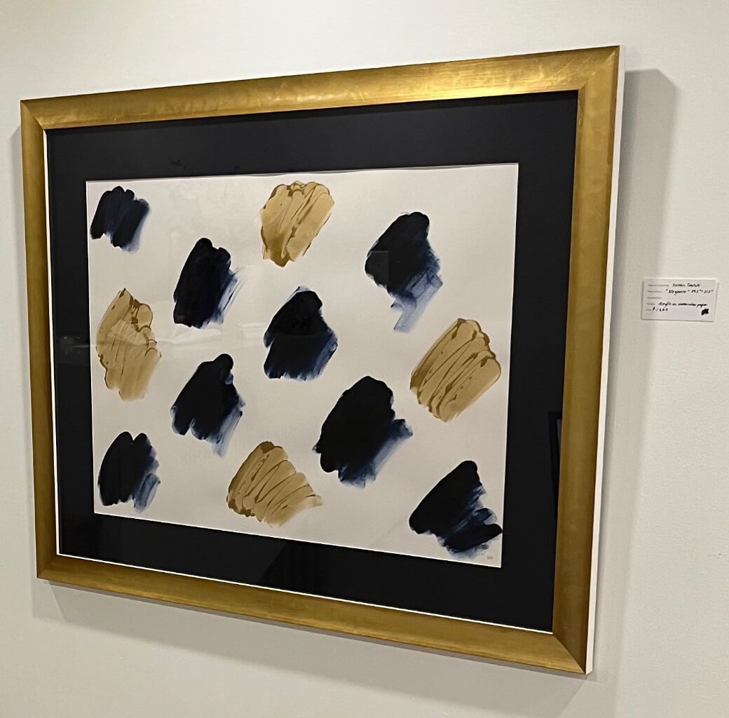 A painting in a gold frame is on a white wall