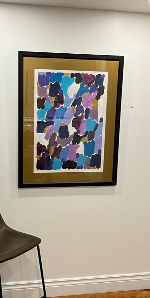 A framed painting is hanging on a white wall next to a chair.