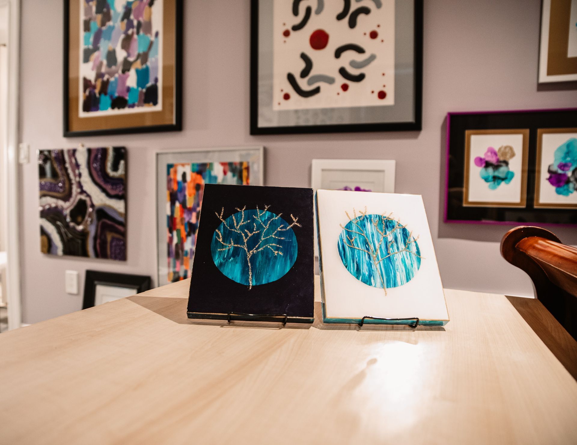 Two paintings are sitting on a table in front of a wall of paintings.