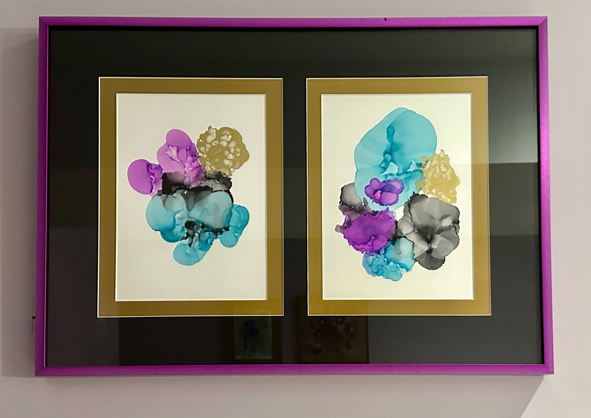 Two paintings in a purple frame are hanging on a wall.