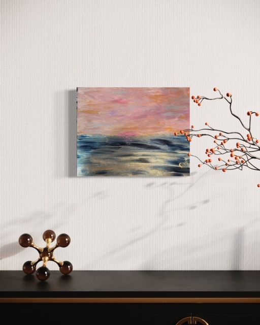 A painting of a sunset over the ocean is hanging on a wall above a table.