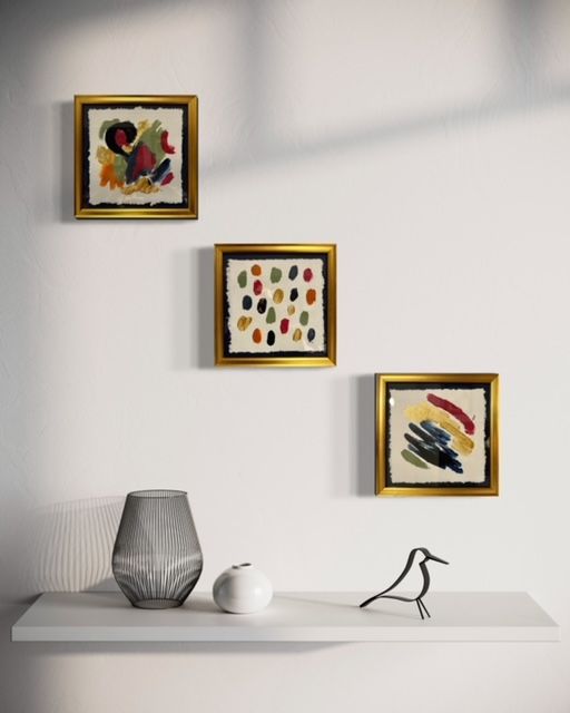 Three paintings are hanging on a wall above a shelf