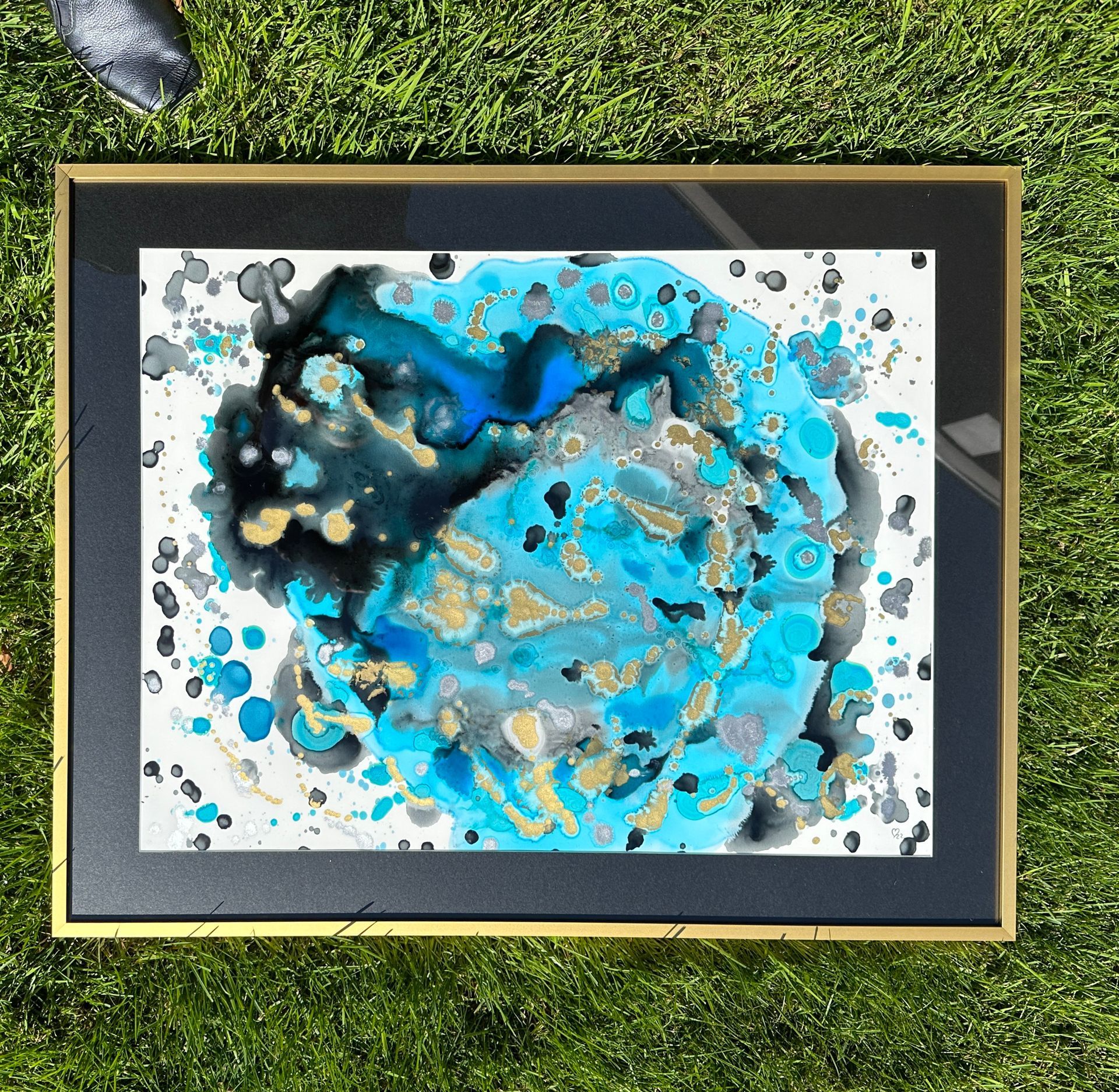 A painting in a black frame is sitting on the grass