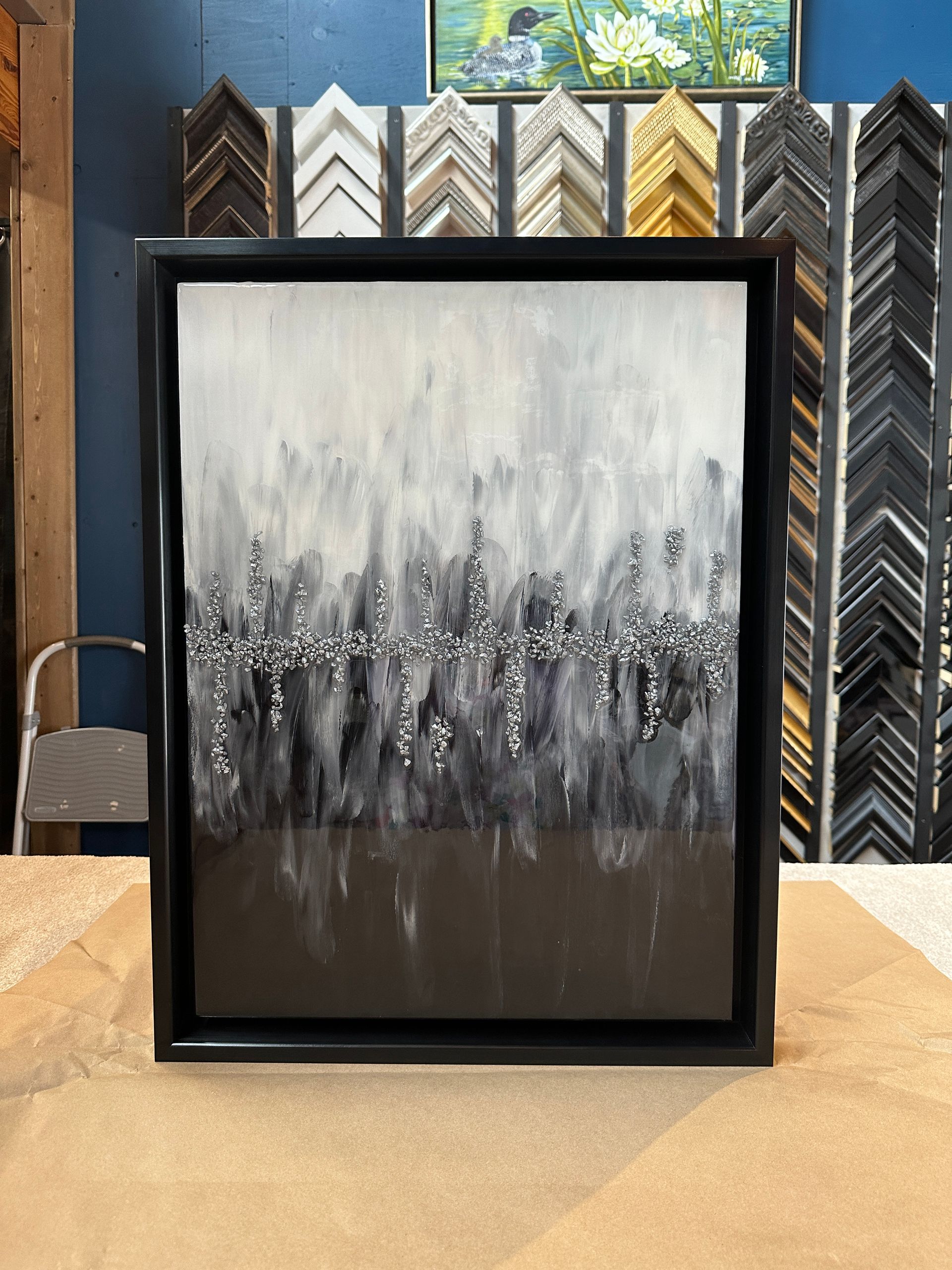 A black and white painting in a black frame is sitting on a table.