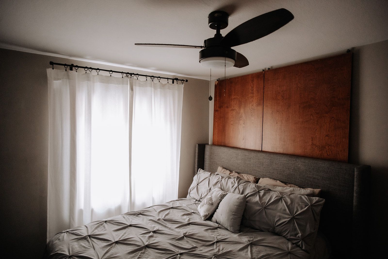 Cozy bedroom. Light filters through curtains from large windows. A modern ceiling fan is over an upholstered bed. South Minneapolis apartments by RightMove Properties.