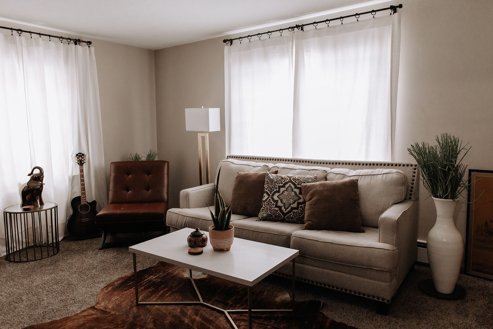 Cozy living room with cute plant and music decorations. Filtered sunlight through curtains. Beige couch and dark brown leather side chair. South Minneapolis apartments by RightMove Properties.