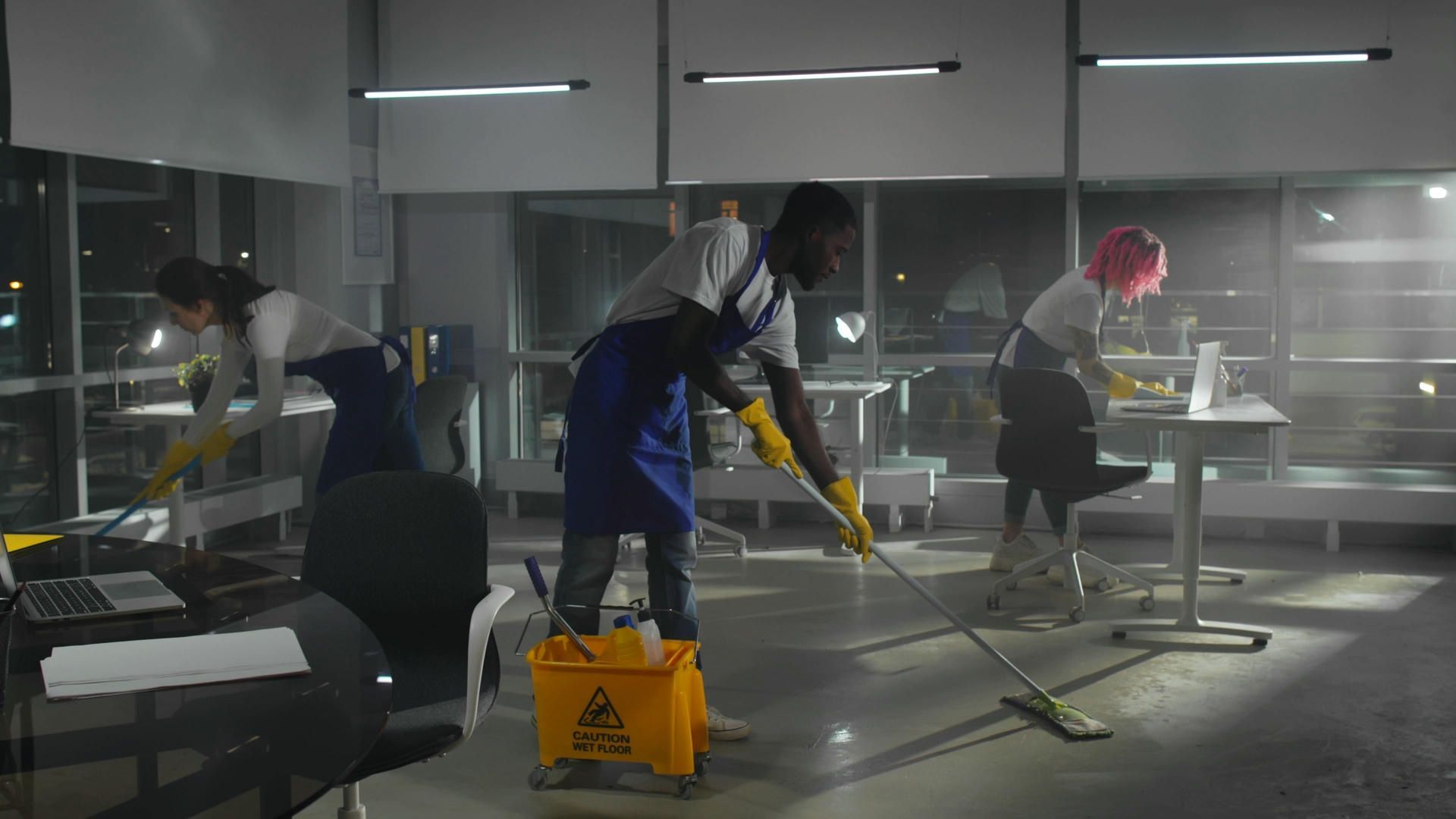 A group of janitors are cleaning an office at night.