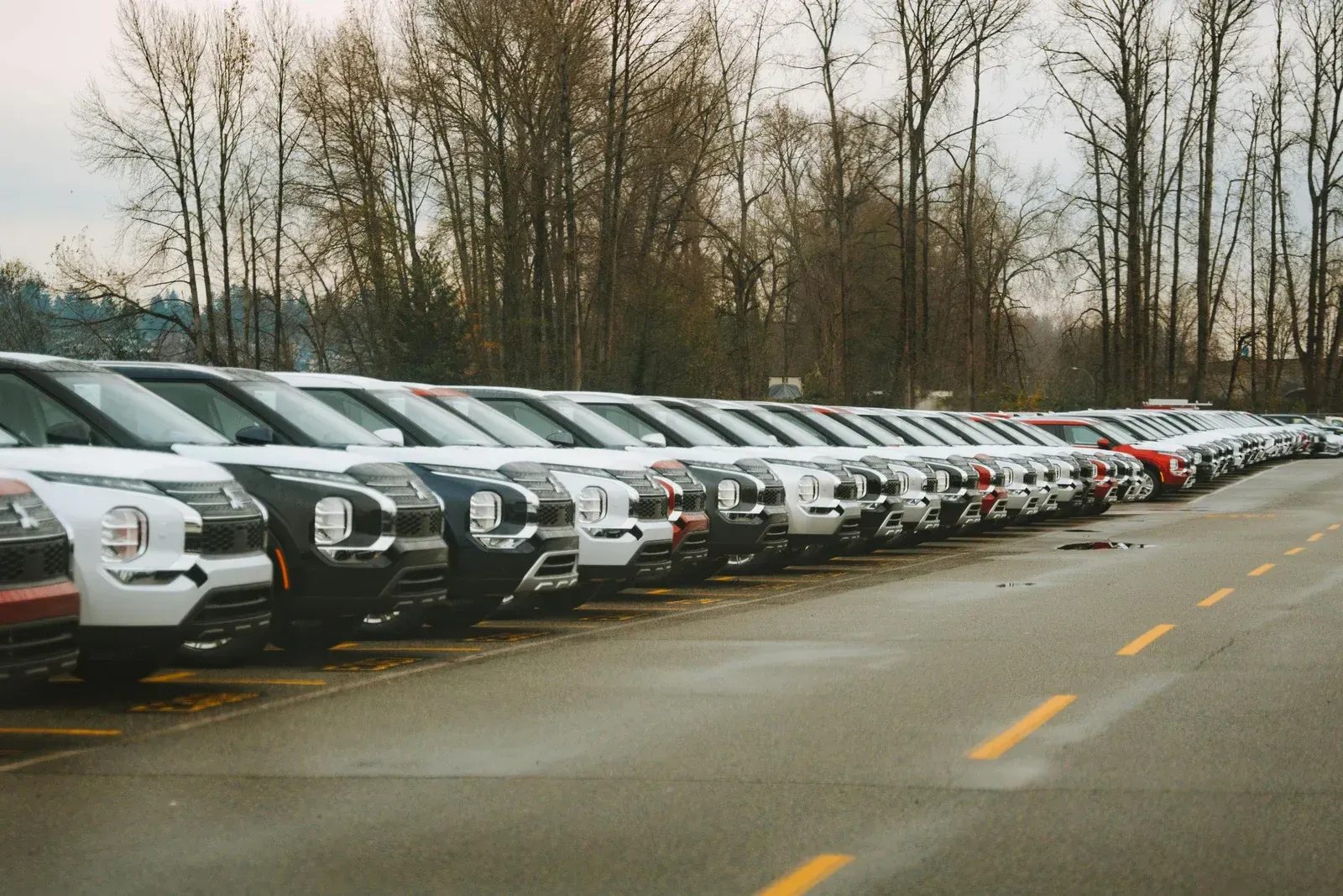 Row of parked new cars in various colors, outdoors.