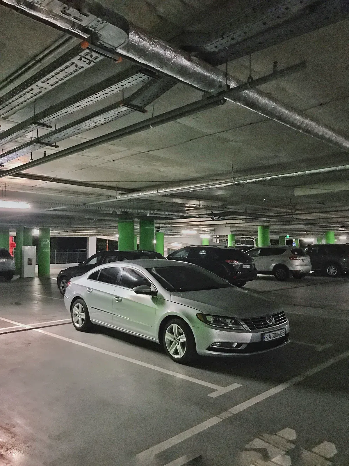 Silver Volkswagen sedan parked in a dim, multi-level parking garage. Other cars are also parked.