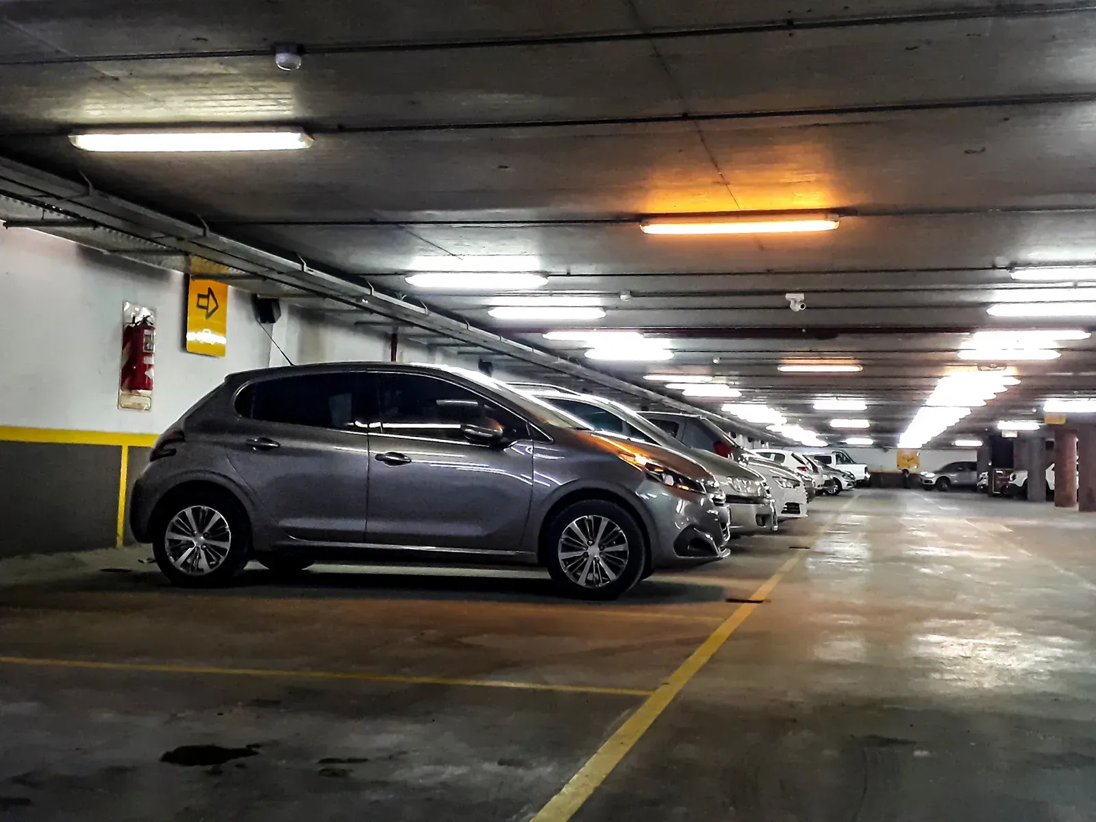Gray cars parked in a concrete parking garage under fluorescent lights.