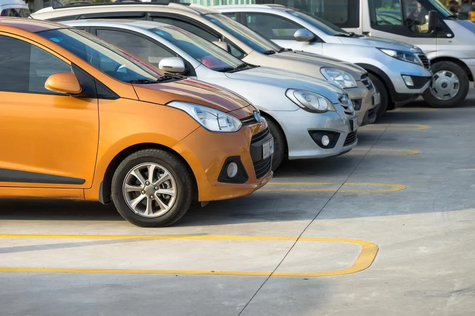Orange car parked in a row with other vehicles on concrete.