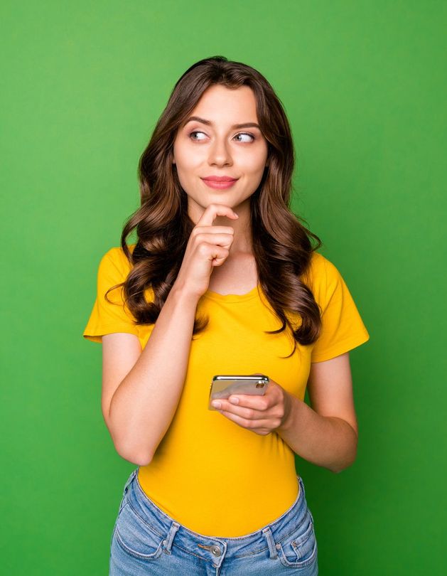 A woman in a yellow shirt is holding a cell phone and thinking.