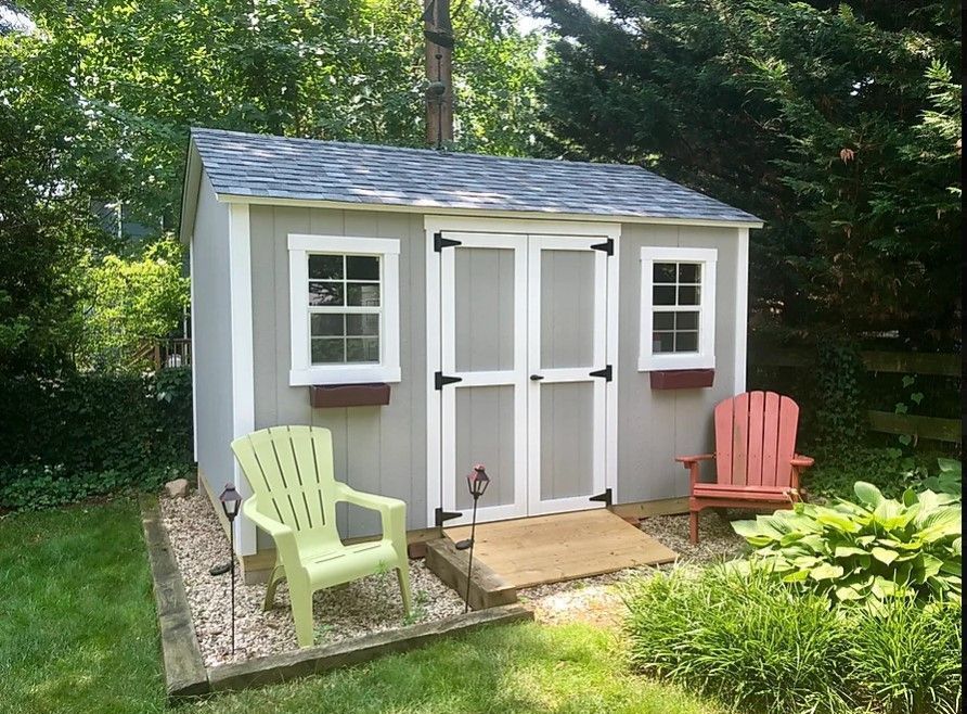 A shed with two green chairs and two red chairs in front of it.