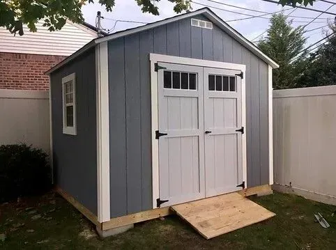 A gray and white shed with a ramp in the backyard.