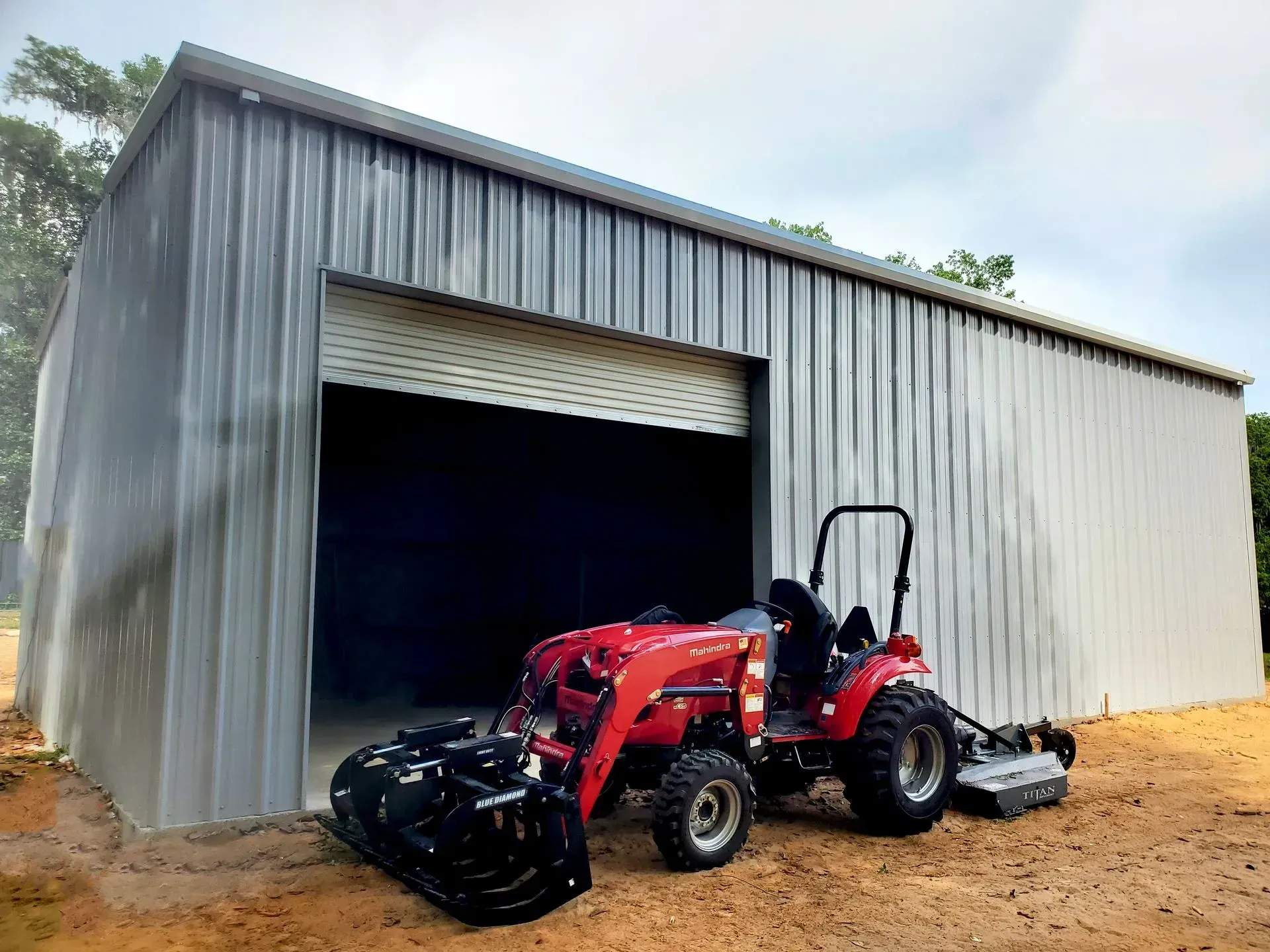 A red tractor is parked in front of a metal garage.