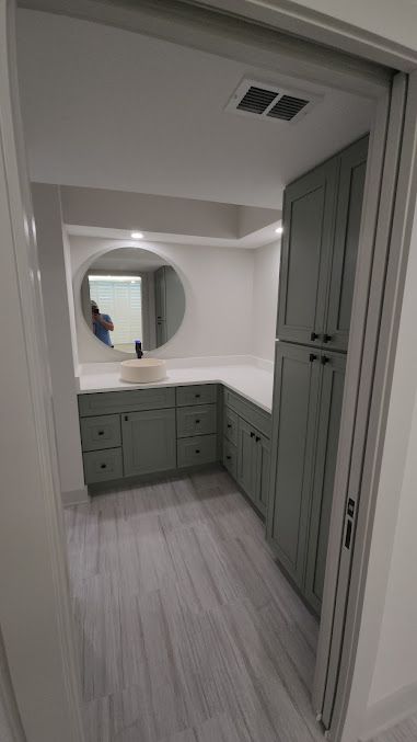 A bathroom with green cabinets and a round mirror.