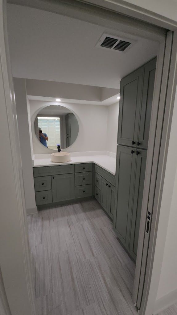 A bathroom with a sink, cabinets, and a round mirror.