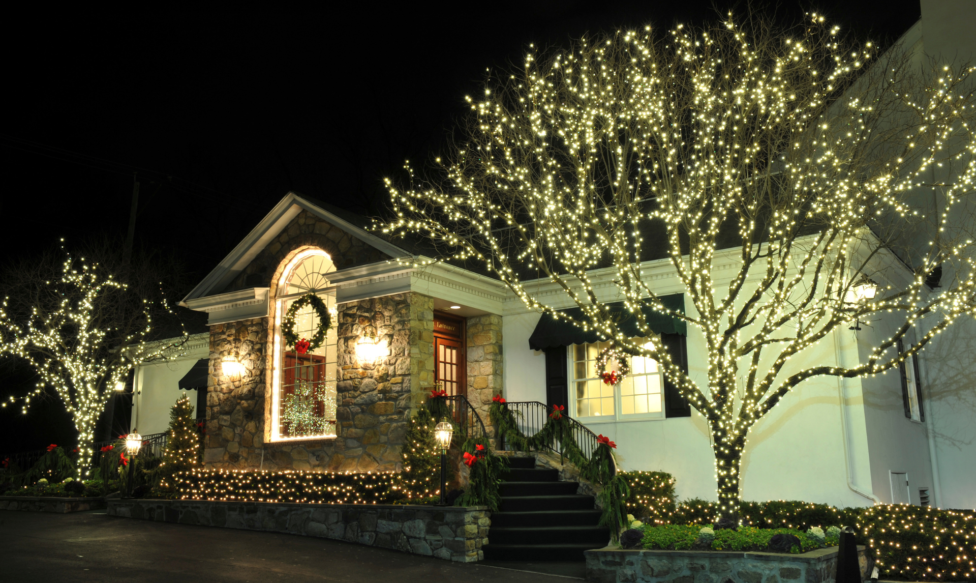 House decorated with Christmas lights and wreaths; illuminated trees.