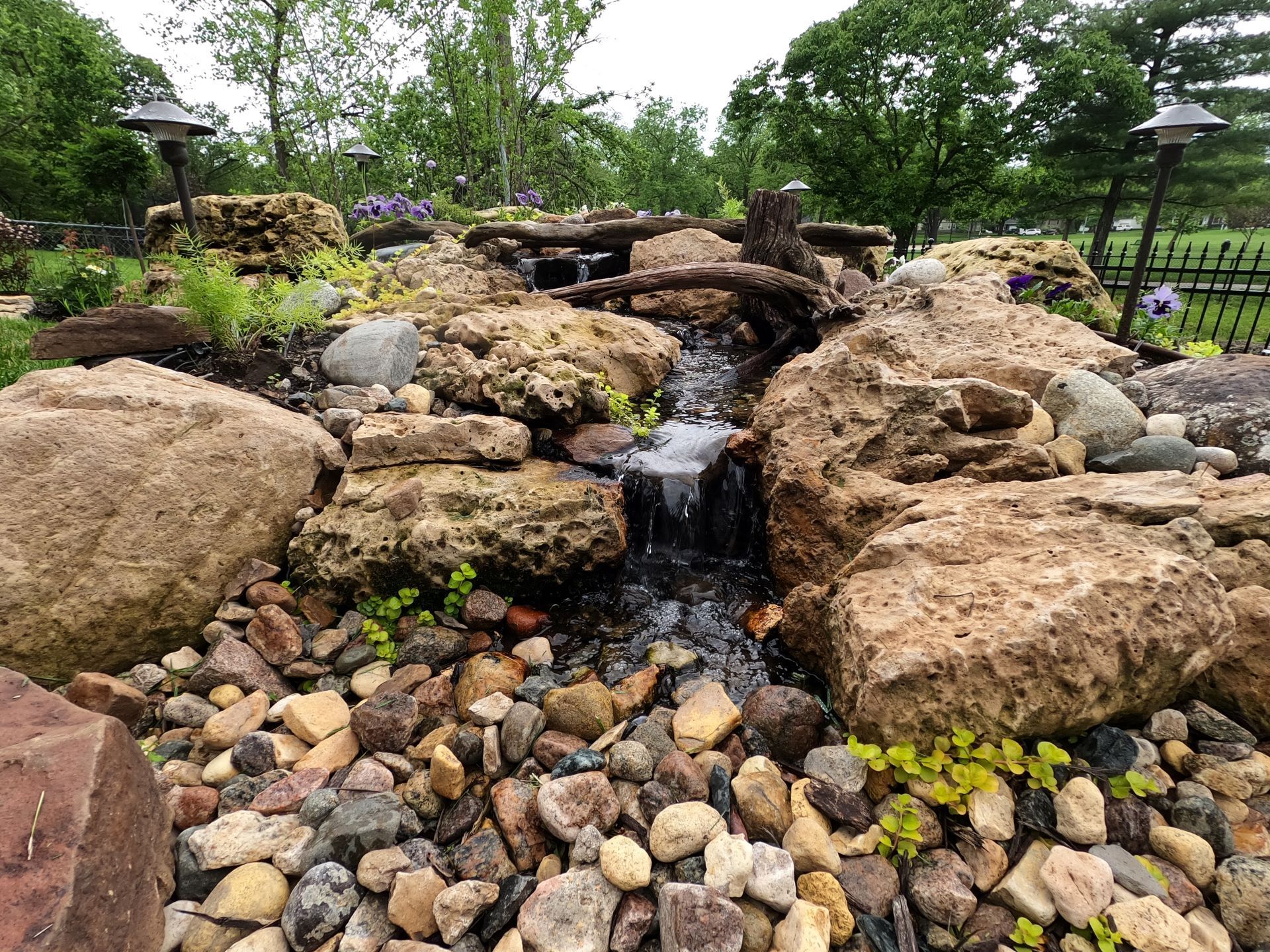 a front yard pondless waterfall running with bushes and trees surrounding.
