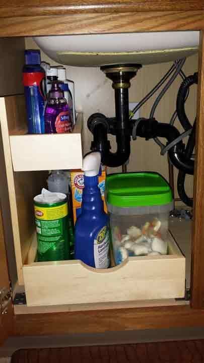 Bathroom cabinet with cleaning supplies, two pull-out shelves around plumbing under a sink.