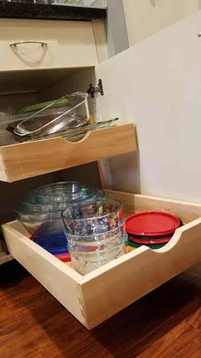 Pull-out drawers in a kitchen cabinet filled with glass bowls and lids. Wooden drawers on a wood floor.